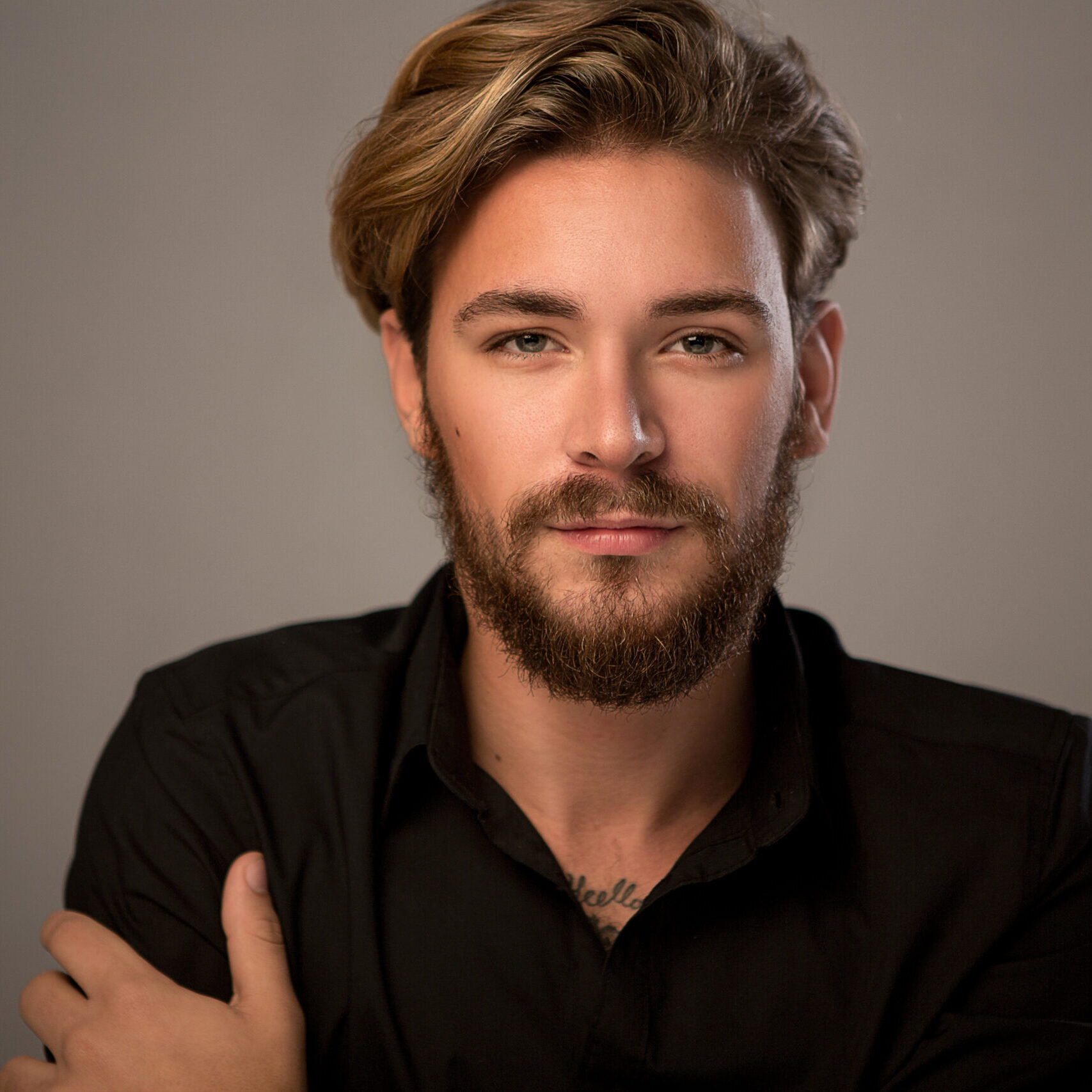 Close up portrait of young caucasian man looking at camera. Wearing  beard and long curly hair. Image is on grey background.