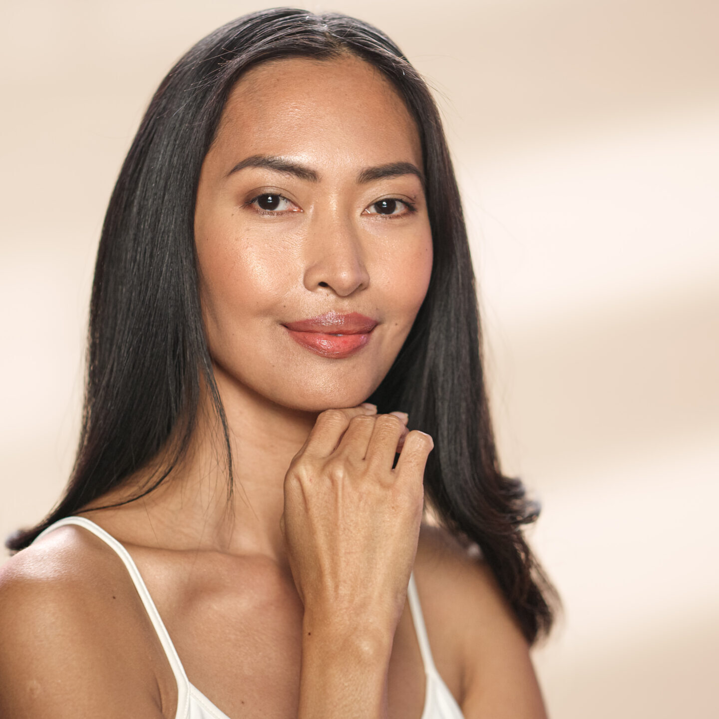 Female Beauty Portrait. Beautiful Asian Happy Brunette Woman Posing, Touching Her Face with Natural, Healthy Skin. Wellness and Skincare Concept on Soft Isolated Background. Close Up.